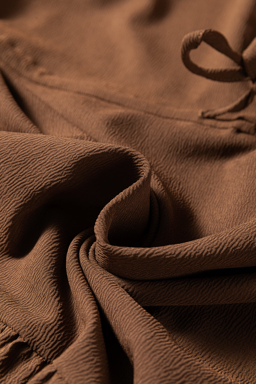 Close-up of brown textured fabric with drawstring detail, soft and wrinkled surface