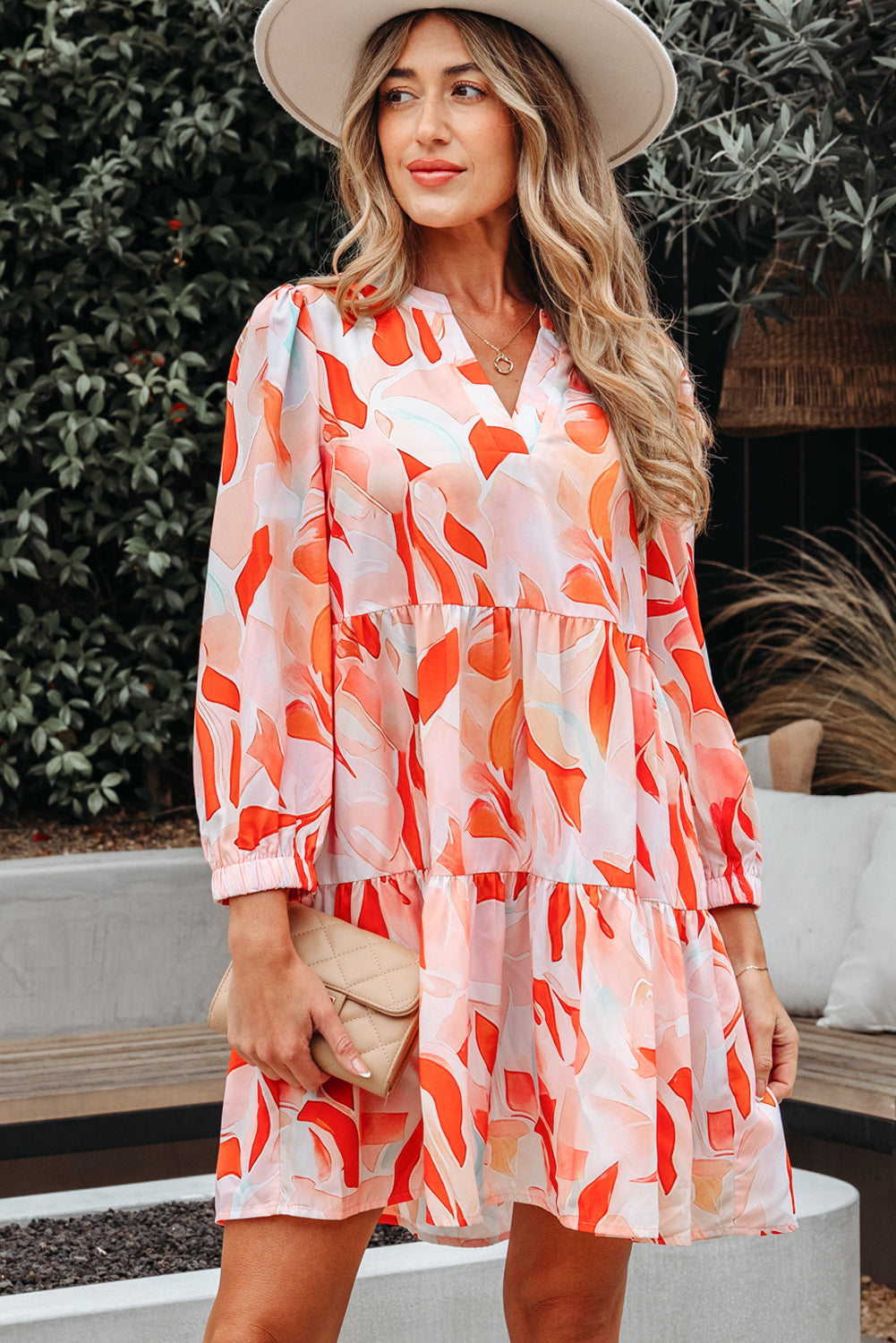 Woman in a colorful abstract print mini dress with long sleeves, holding a beige clutch