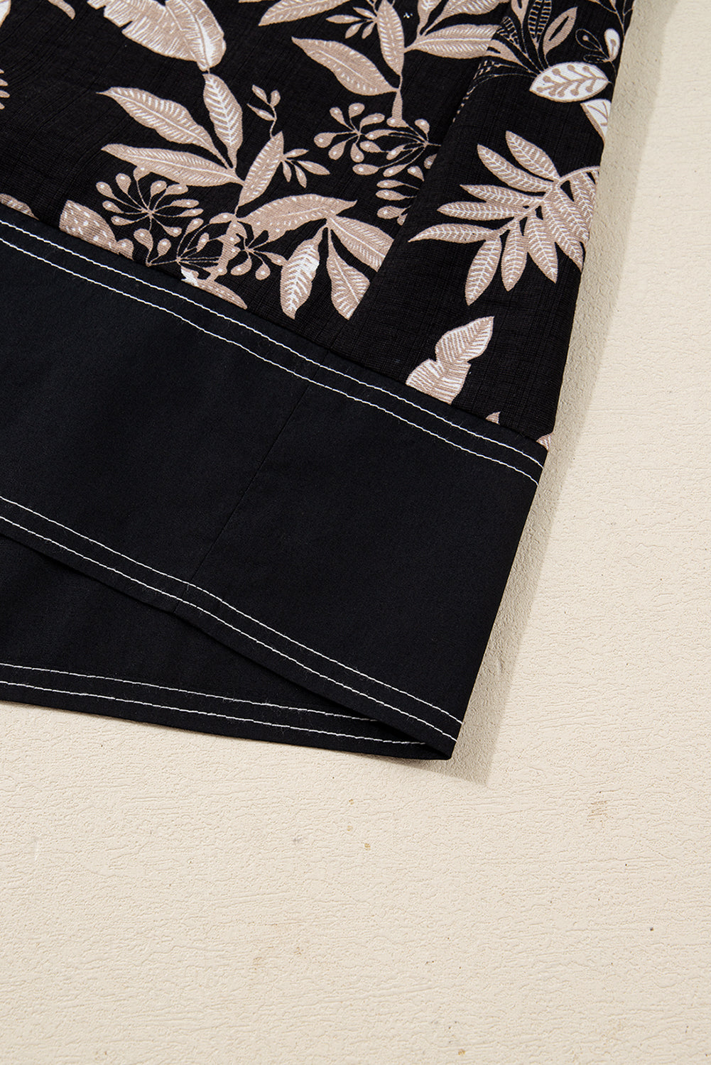 Close-up of black sleeve with beige leaf print and contrasting stitched cuff