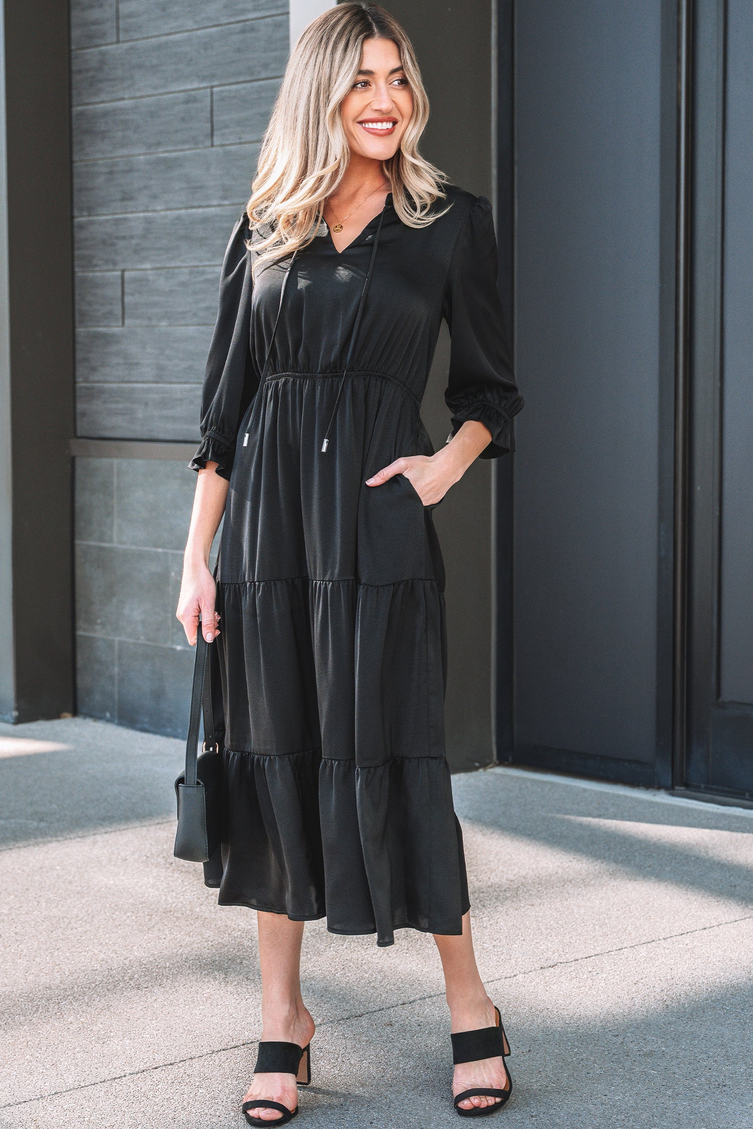 Woman wearing a black midi dress with long sleeves, ruffle details, and black sandals