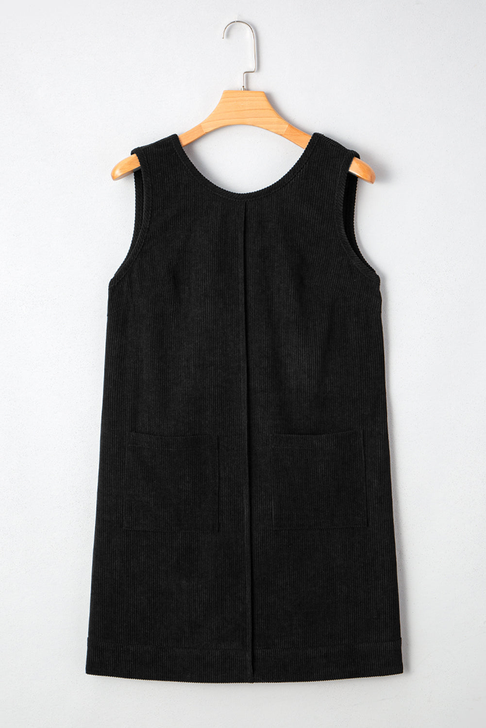 Black corduroy sleeveless shift dress with front pockets on wooden hanger