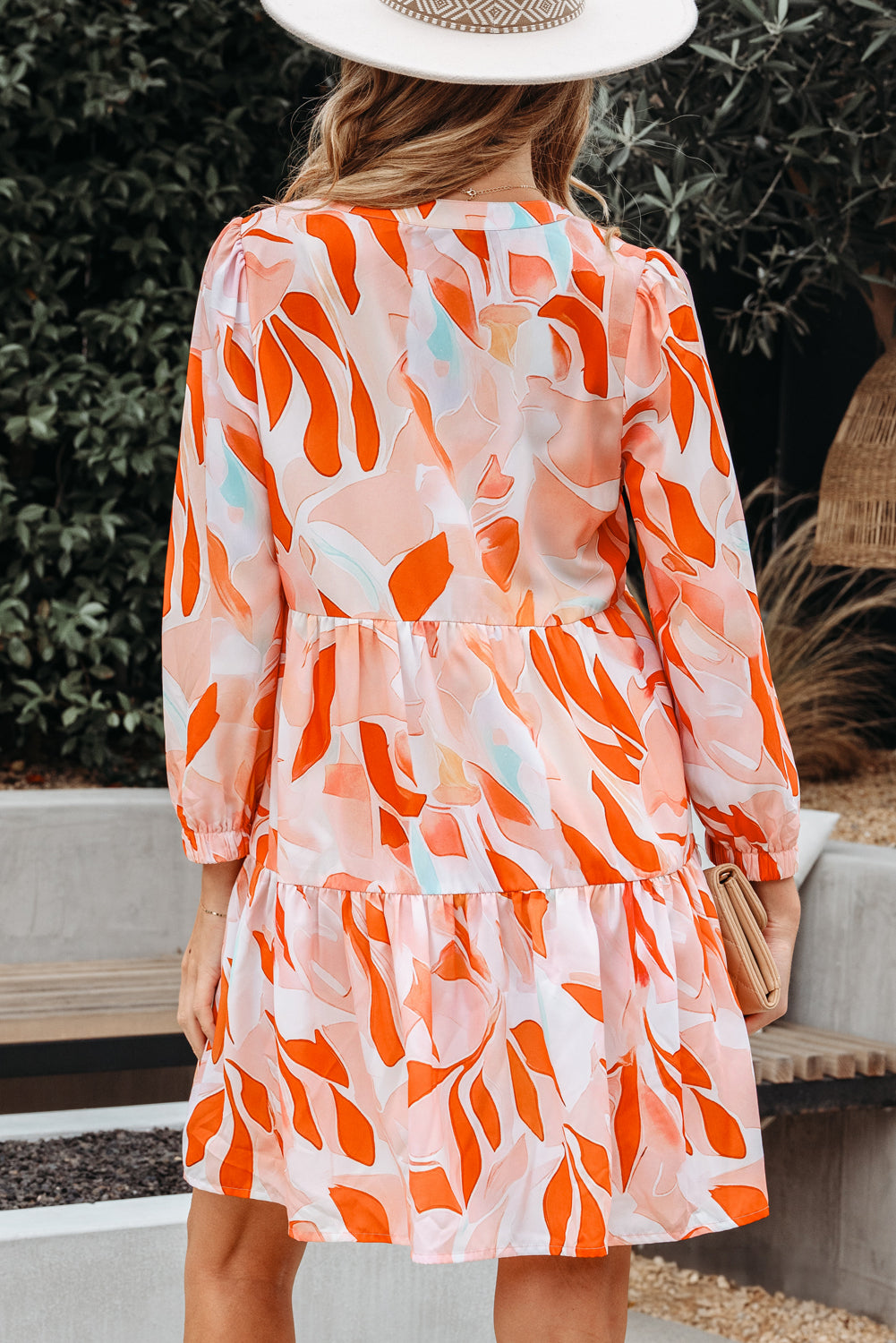 Woman in a long sleeve, orange and pink abstract print dress with white hat outdoors
