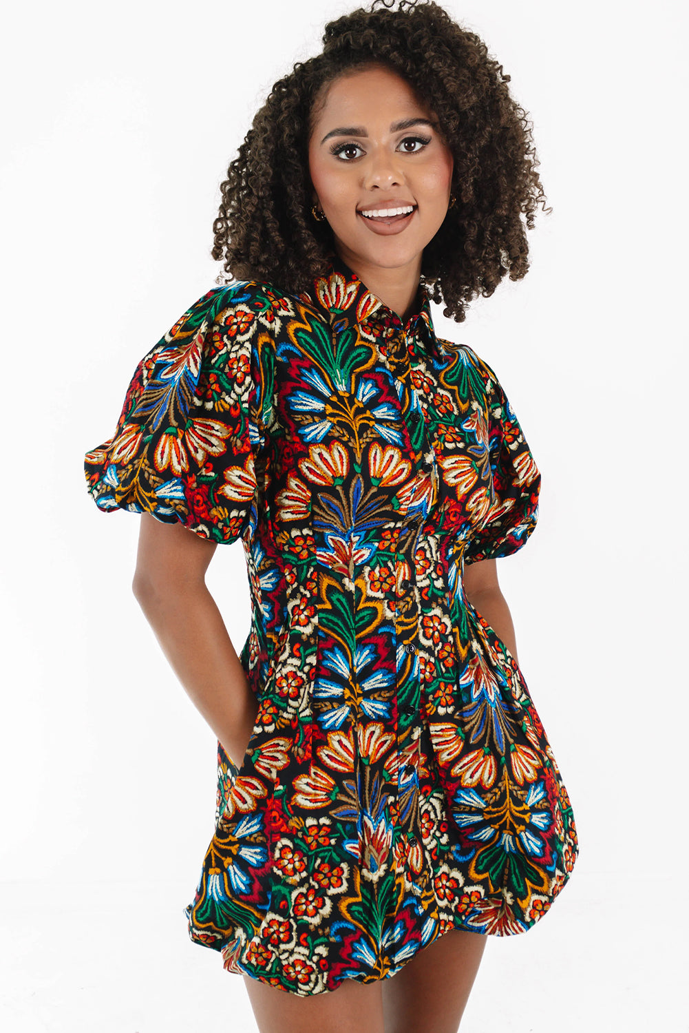 Woman wearing colorful floral puff sleeve dress, smiling against white background