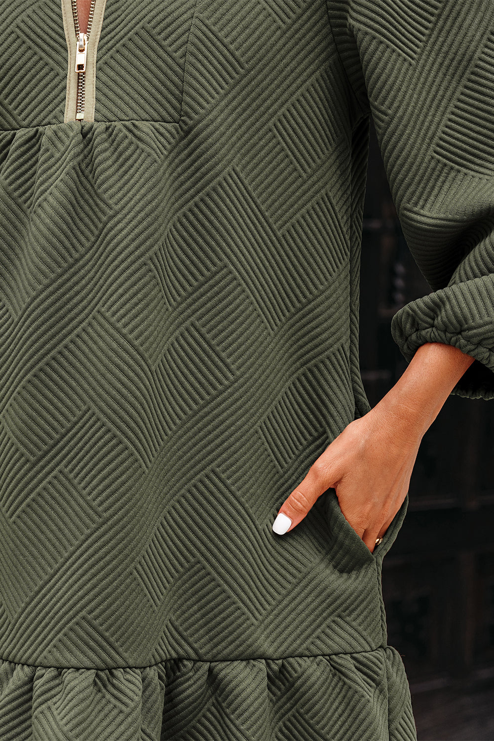 Close-up of a textured olive green dress with a gold zipper and pocket detail