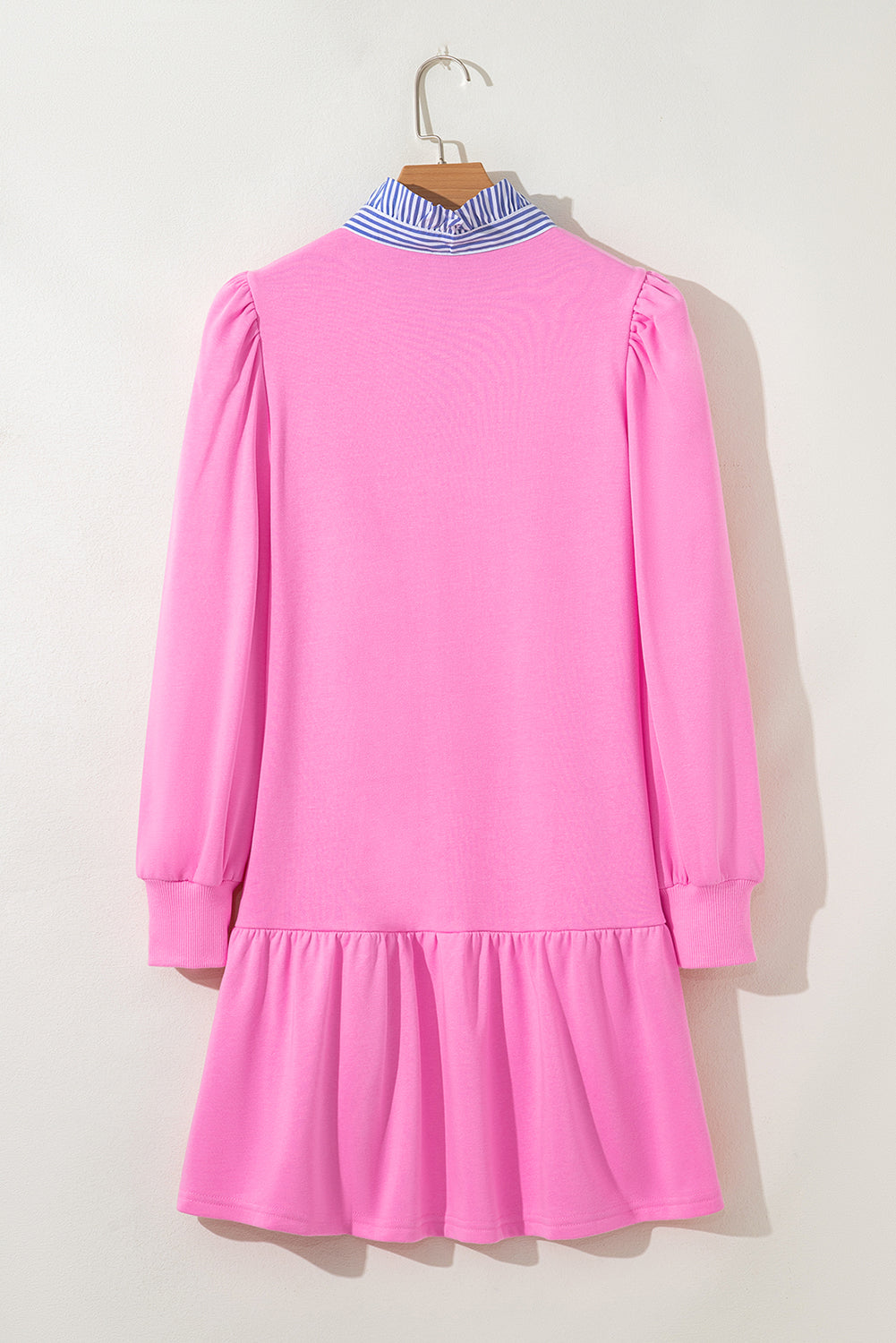 Pink long sleeve dress with ruffle hem and blue striped collar, hanging on a hanger