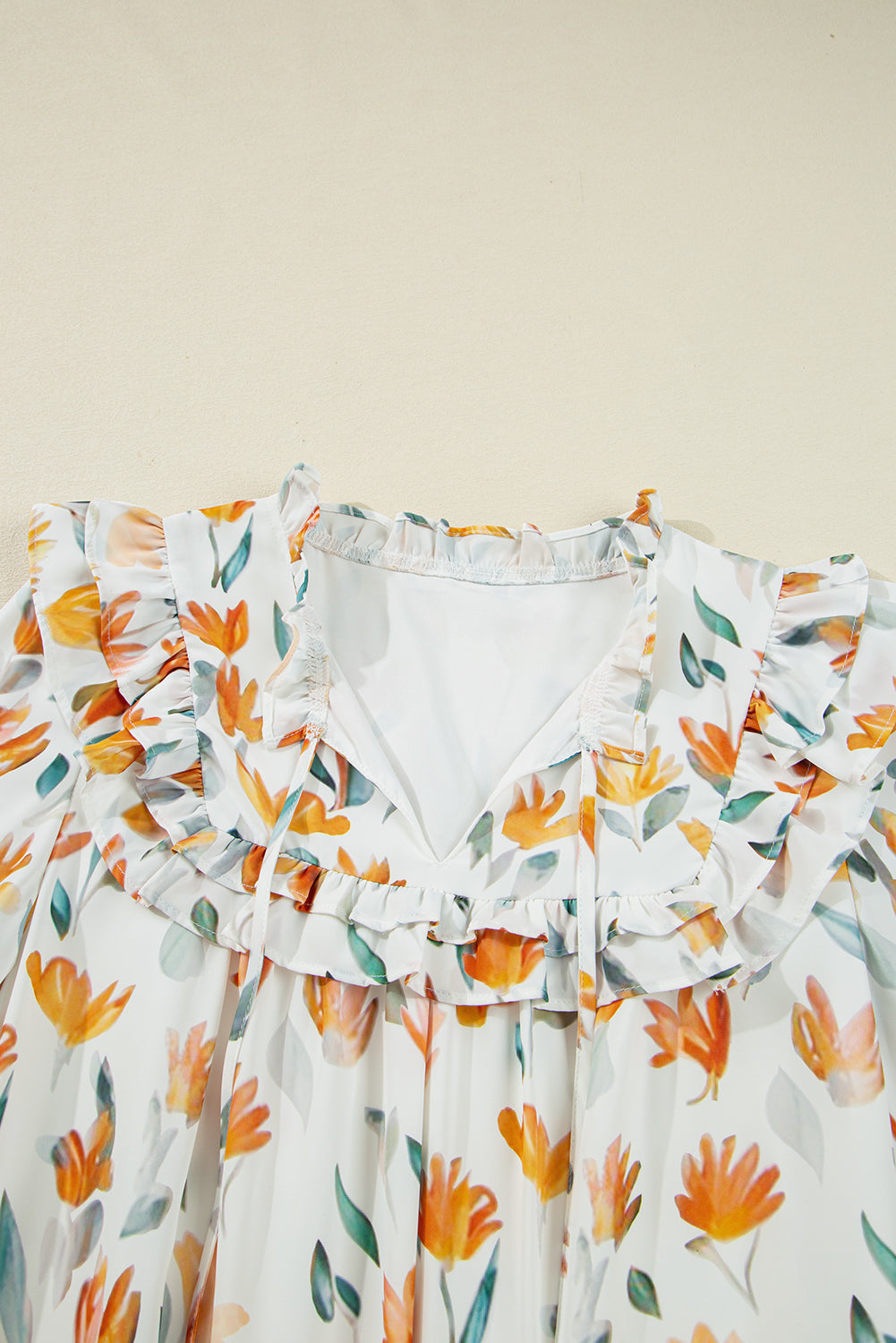 White floral ruffle blouse with orange and green flower print, close-up of neckline
