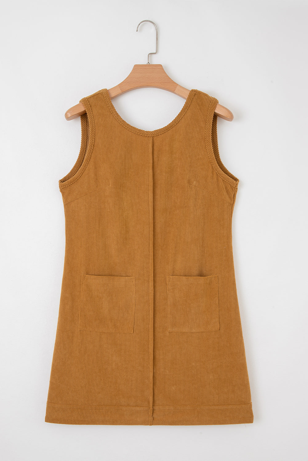 Sleeveless corduroy dress in camel brown with front pockets, hanging on a wooden hanger