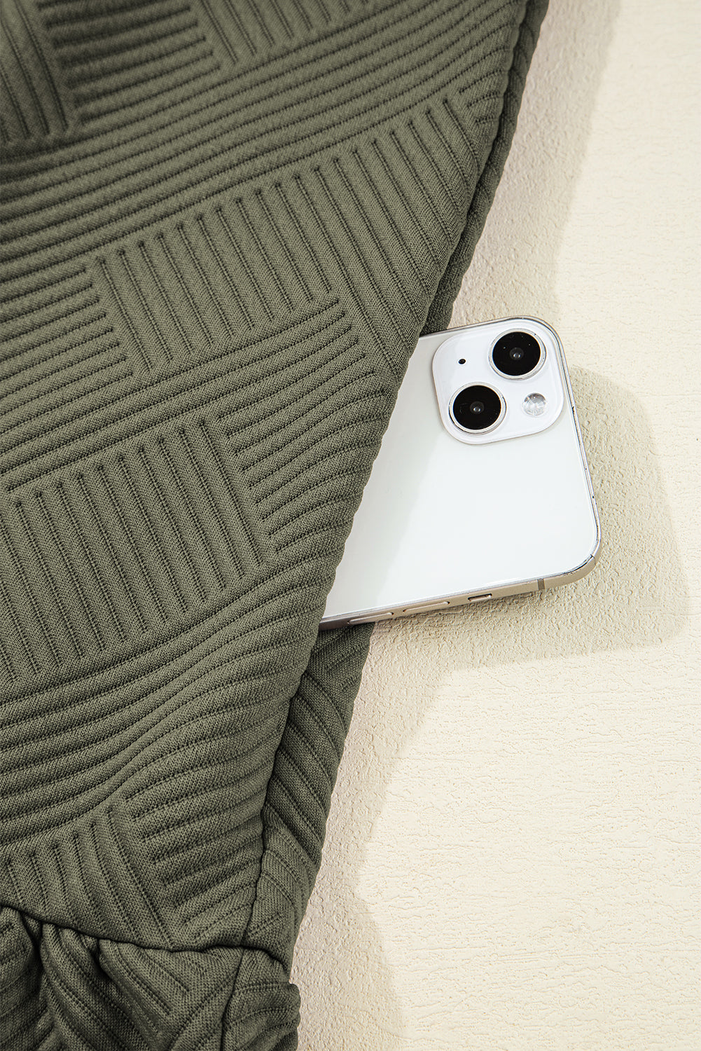 Closeup of green textured pants pocket with white smartphone partially visible