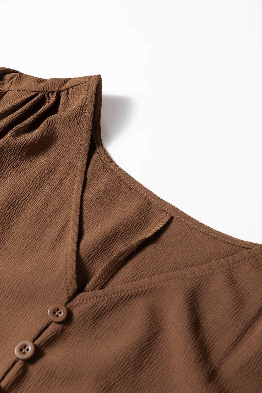 Close-up of brown textured V-neck blouse with buttons and gathered shoulder detail