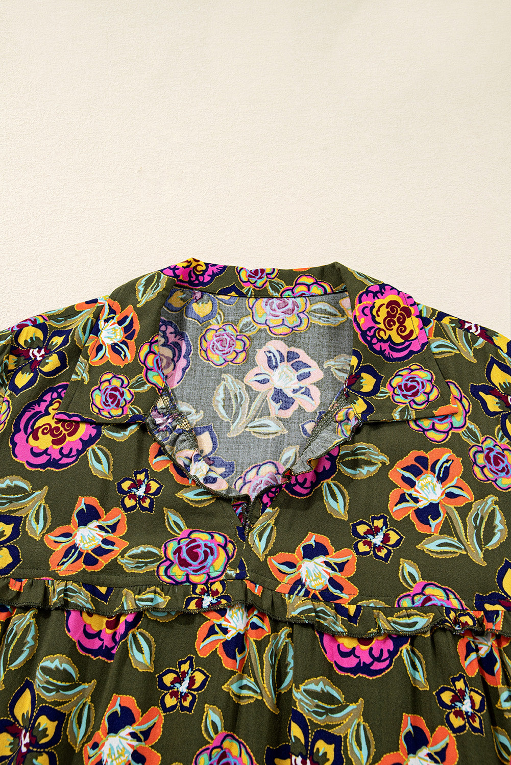 Close-up of floral print dress with ruffle trim and V-neck on olive green fabric