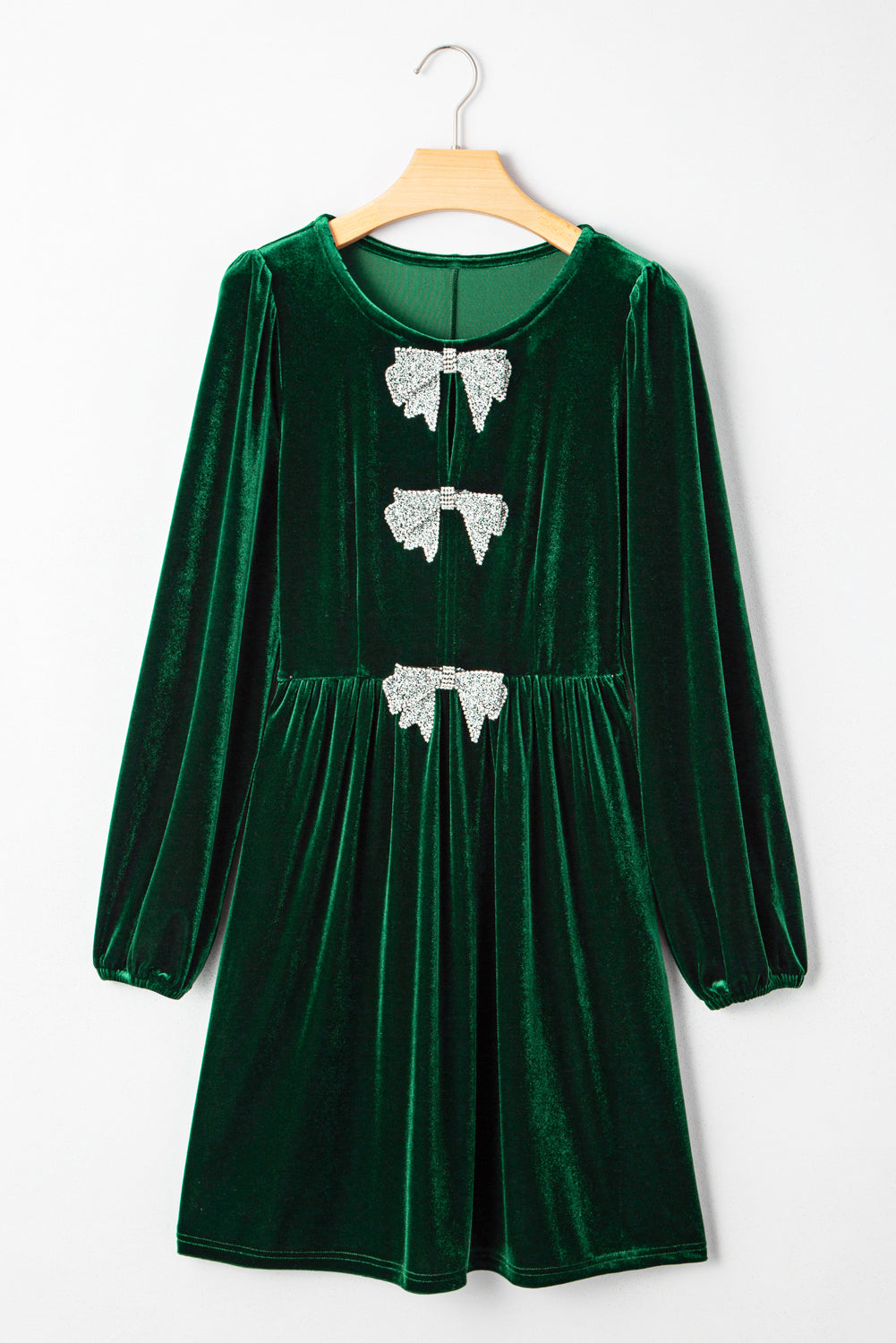 Green velvet long sleeve dress with three silver sequin bows on the front, hanging on a hanger