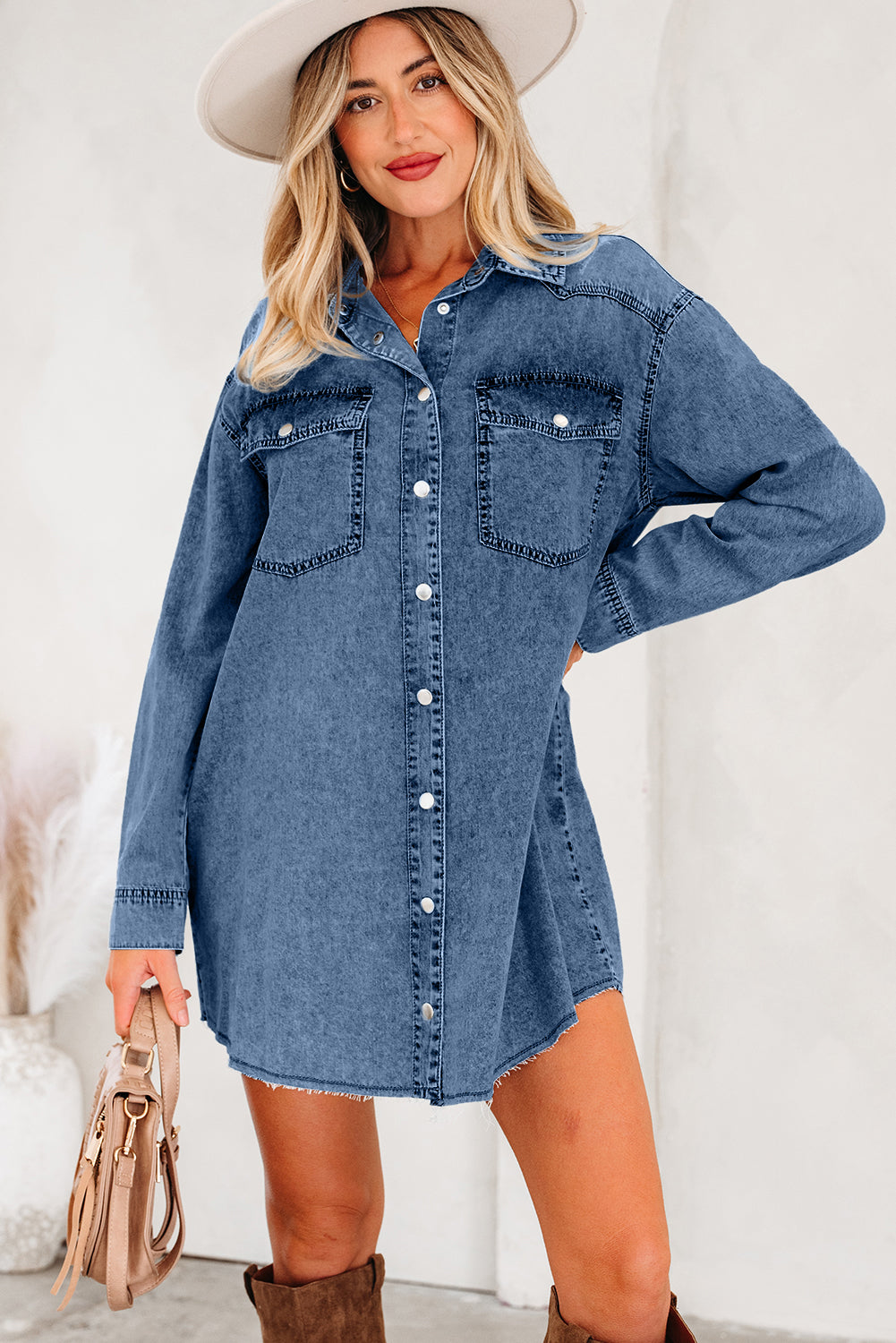 Woman wearing blue denim shirt dress with long sleeves, white hat, and brown boots
