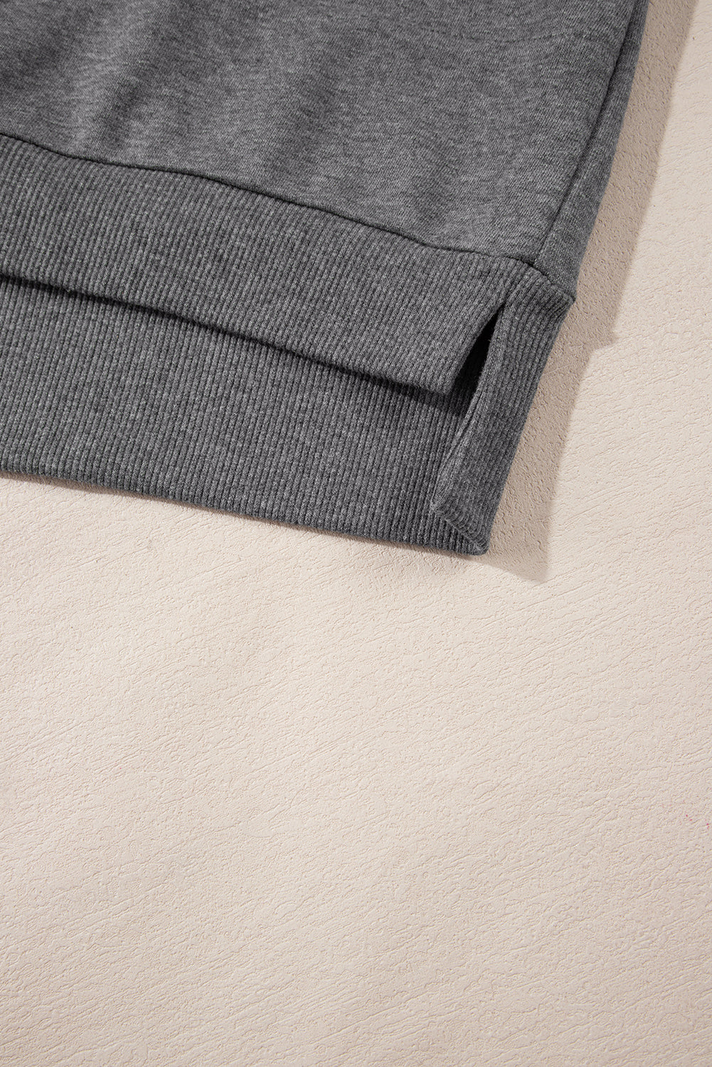 Close-up of gray ribbed sweatshirt hem with side slit on beige textured surface