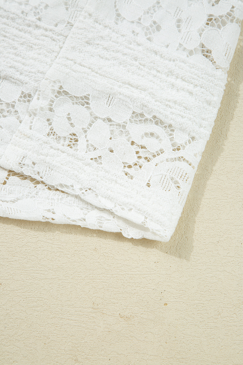 White floral lace fabric with delicate pattern, close-up on light textured surface