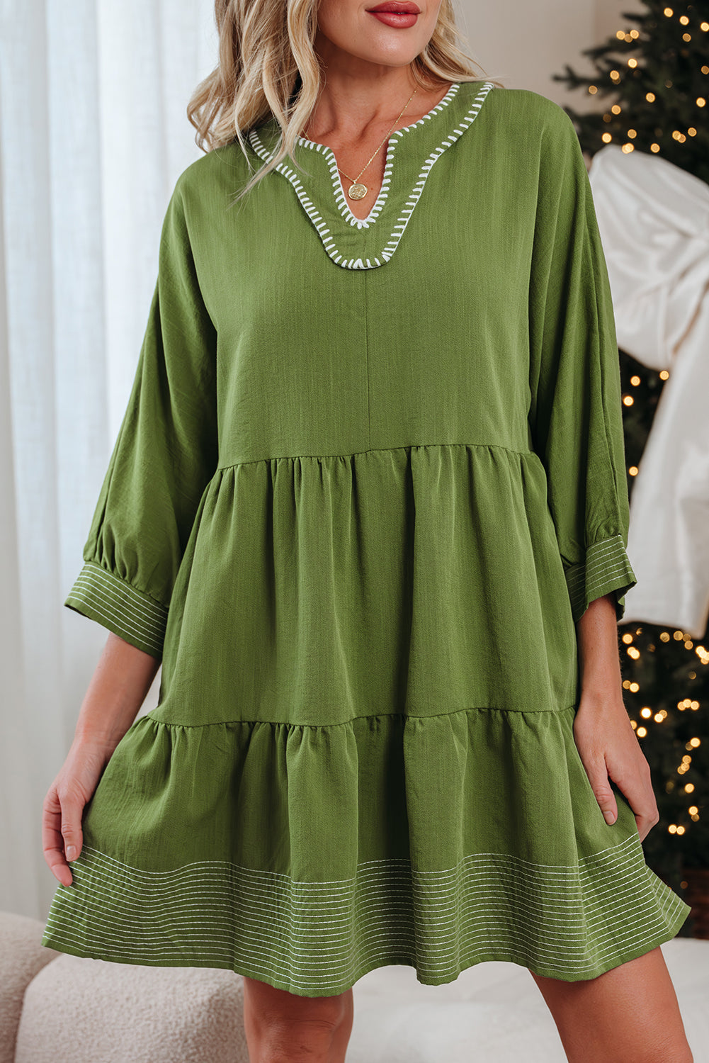 Woman wearing a green tiered long-sleeve dress with white embroidered neckline detail