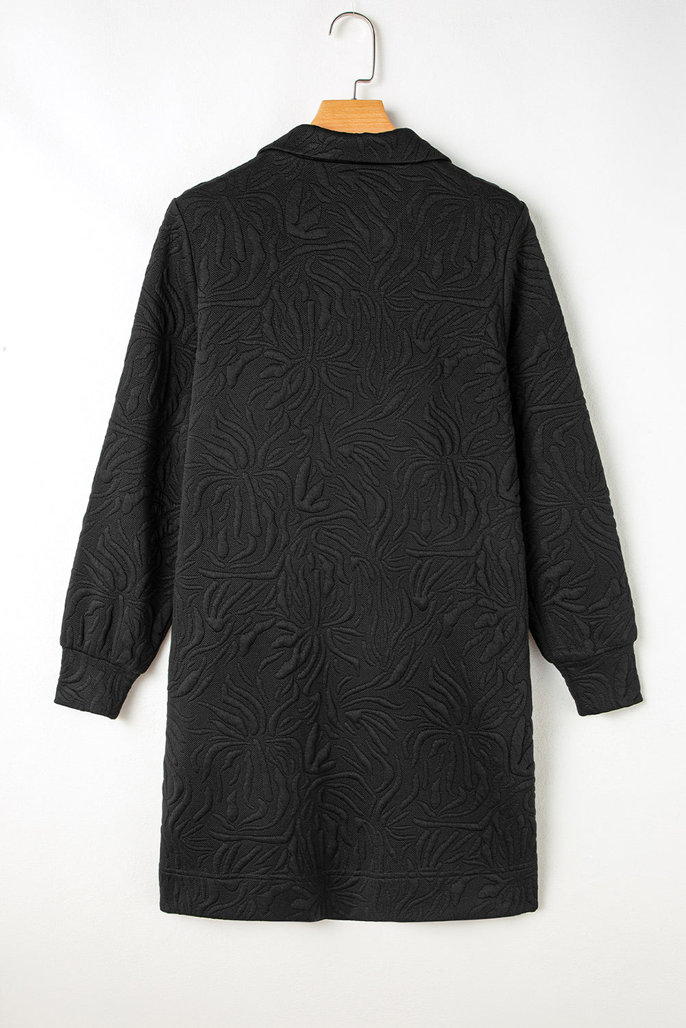 Textured black long-sleeve coat with floral pattern, back view, hanging on wooden hanger