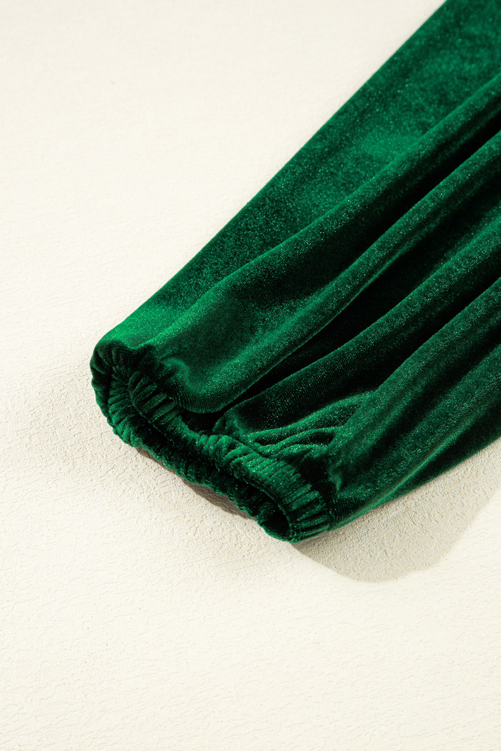 Close-up of green velvet sleeve with elastic cuff on light textured background