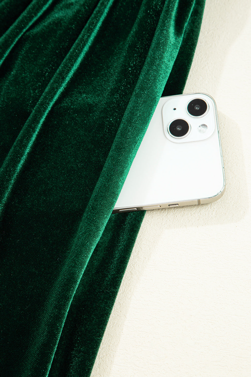 White smartphone in pocket of emerald green velvet fabric, minimal backdrop