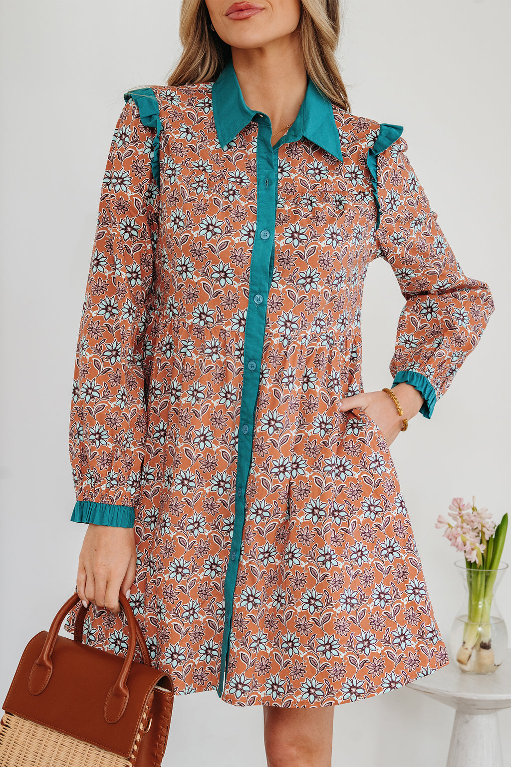 Woman wearing a floral print long sleeve dress with teal collar and holding a brown handbag