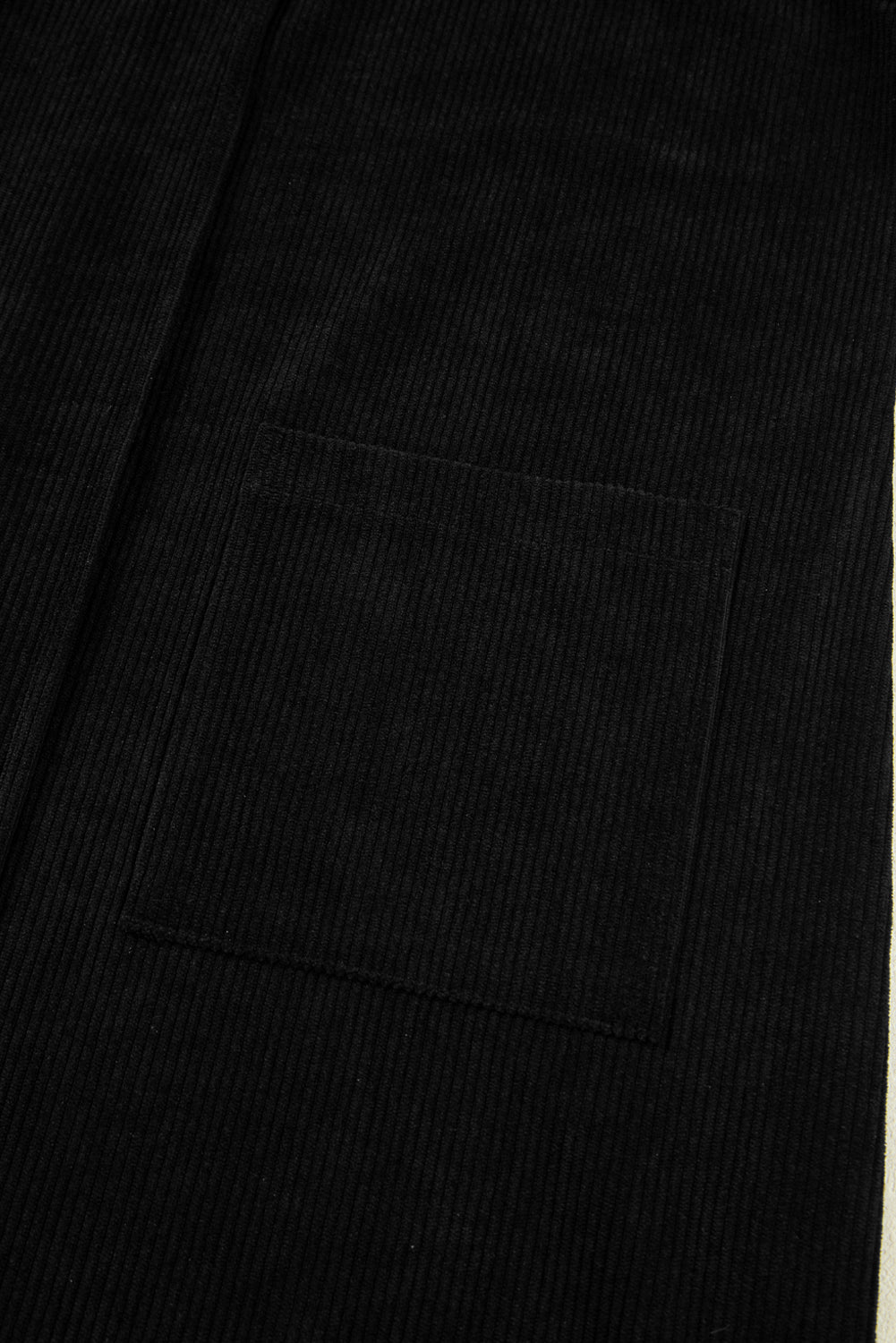 Black corduroy fabric with visible patch pocket and vertical ribbed texture