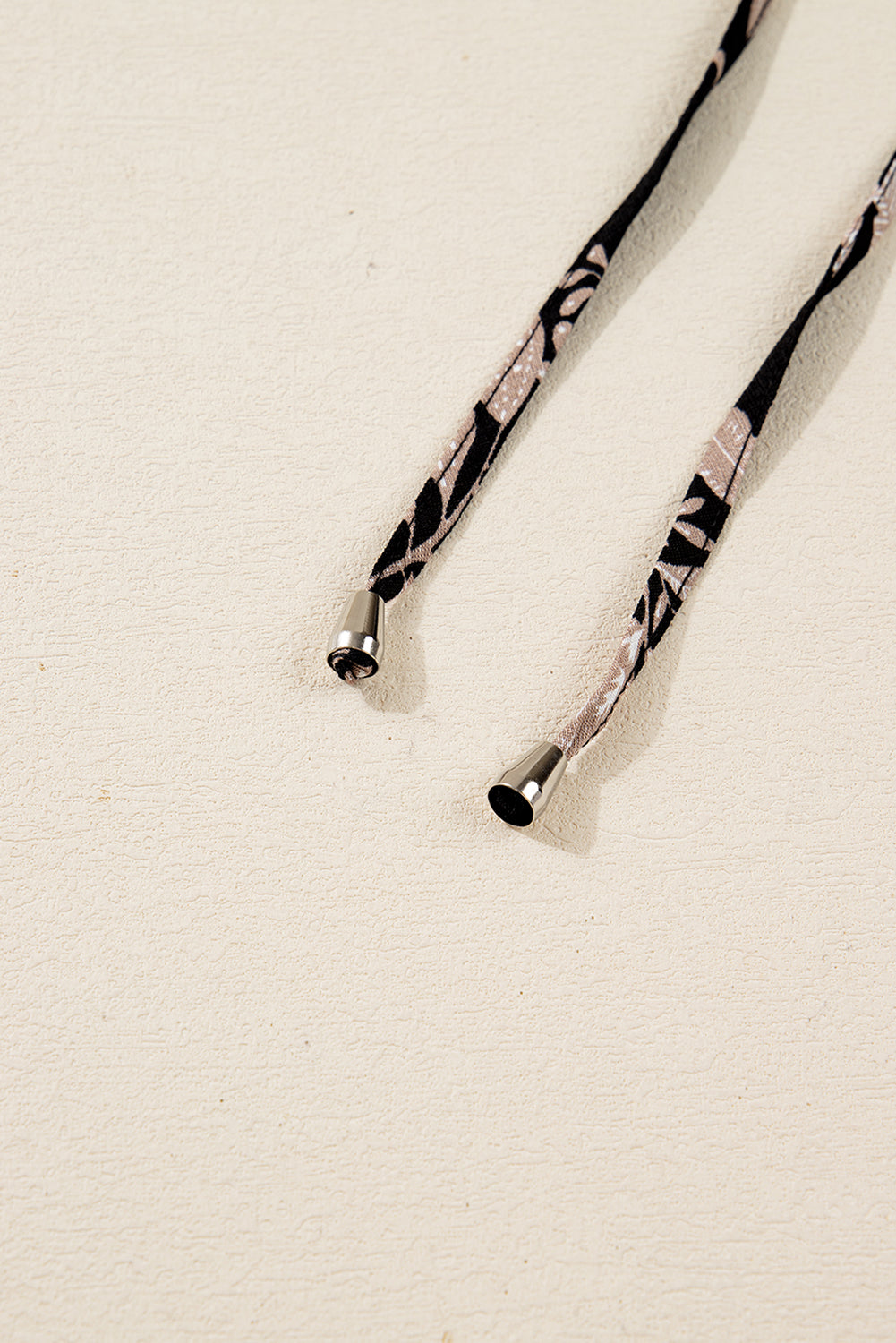 Close-up of patterned fabric drawstrings with metal aglets on a textured beige background