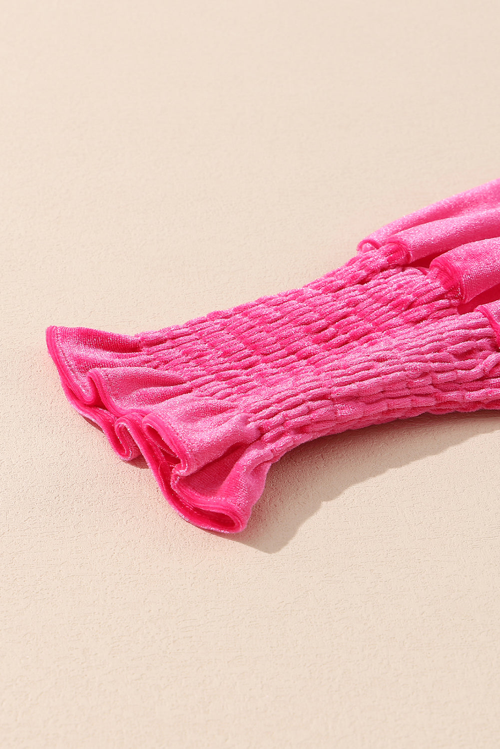 Close-up of pink velvet ruched sleeve with ruffled cuff on neutral background
