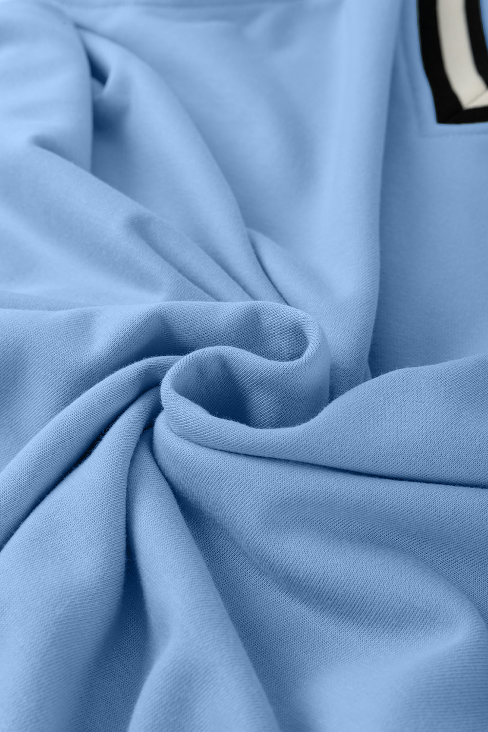 Soft light blue cotton fabric with gentle folds and a visible black and white trim.