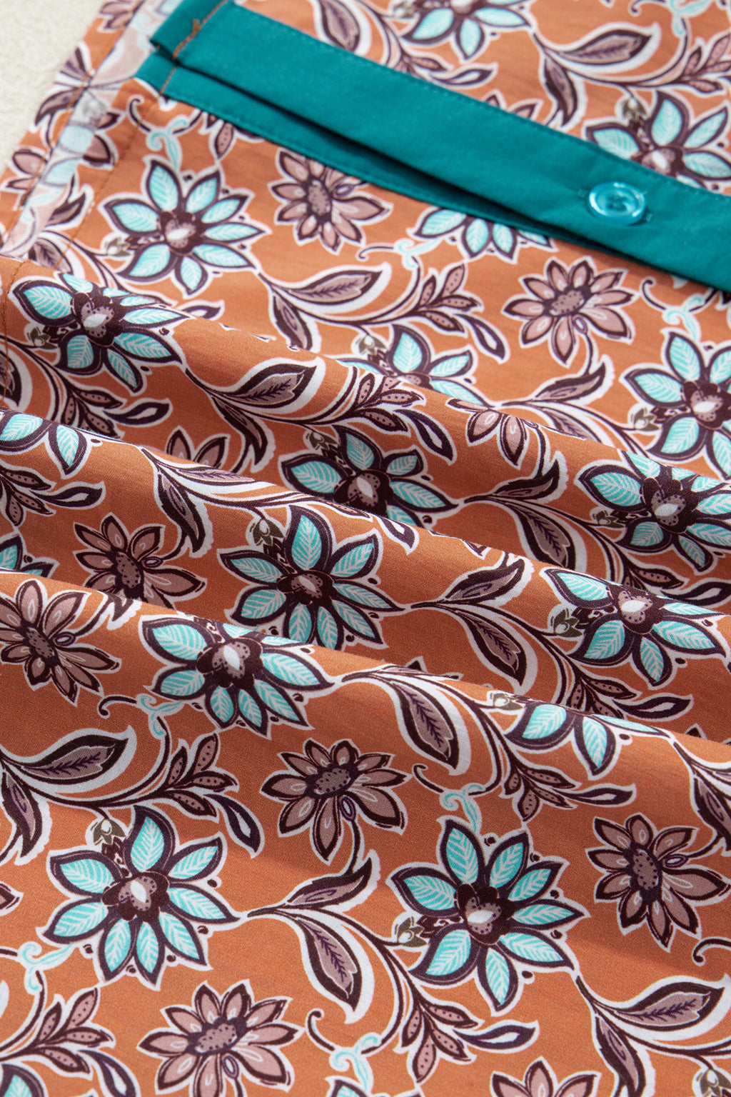 Brown fabric with turquoise buttoned pocket and floral pattern, close-up textile detail