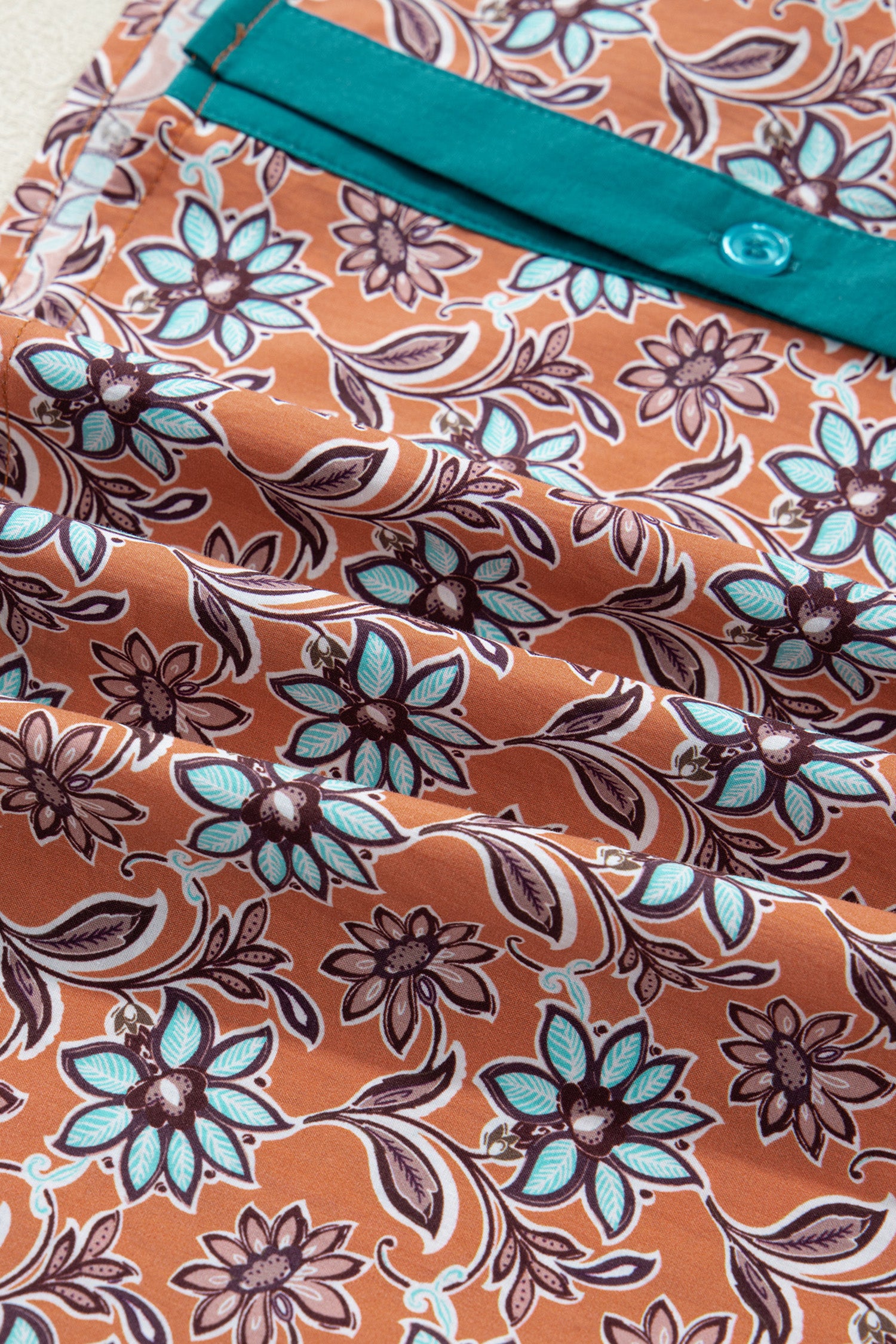 Brown fabric with turquoise buttoned pocket and floral pattern, close-up textile detail