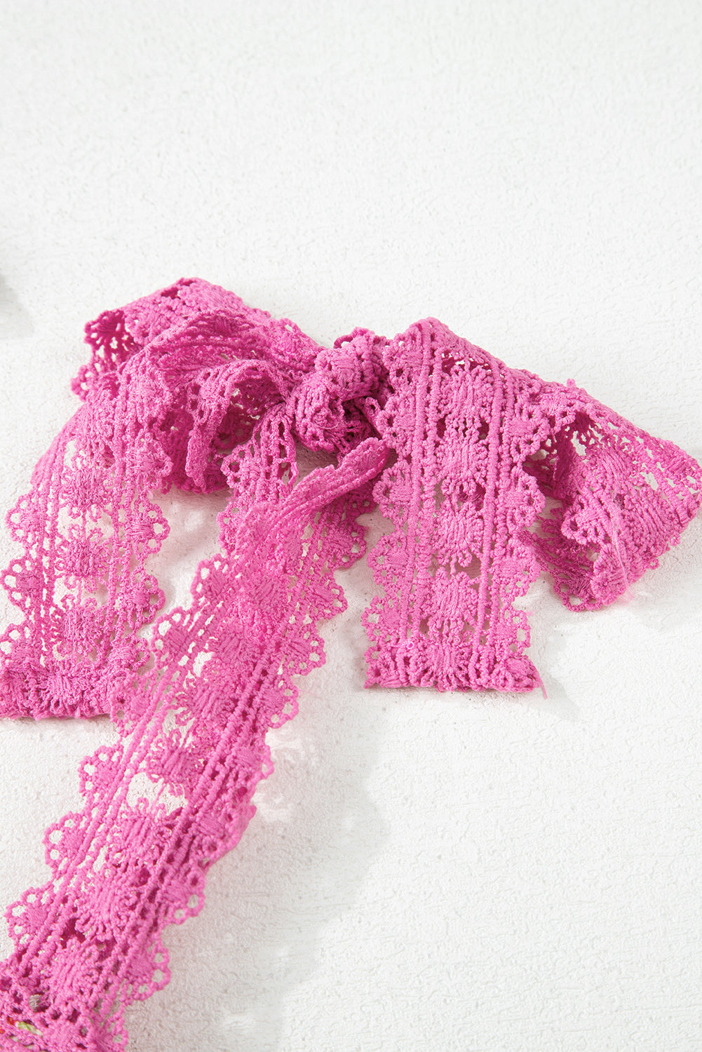 Pink lace ribbon with intricate floral pattern arranged in a bow on white background