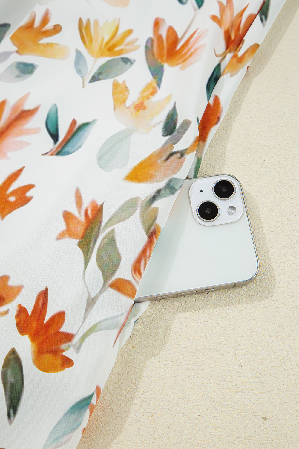 White smartphone partially hidden under floral fabric with orange and yellow flowers
