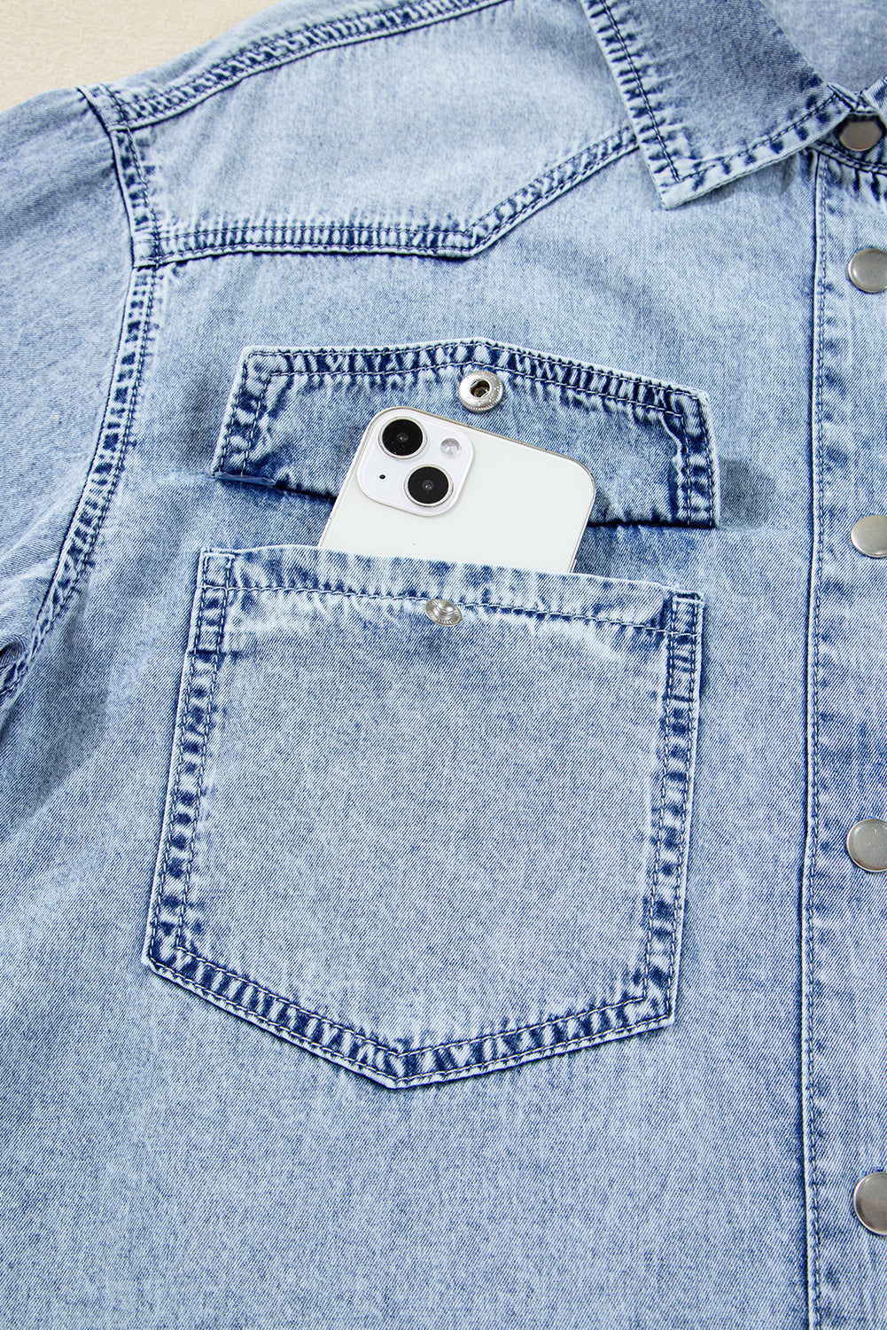Light blue denim shirt with front pocket holding a white smartphone