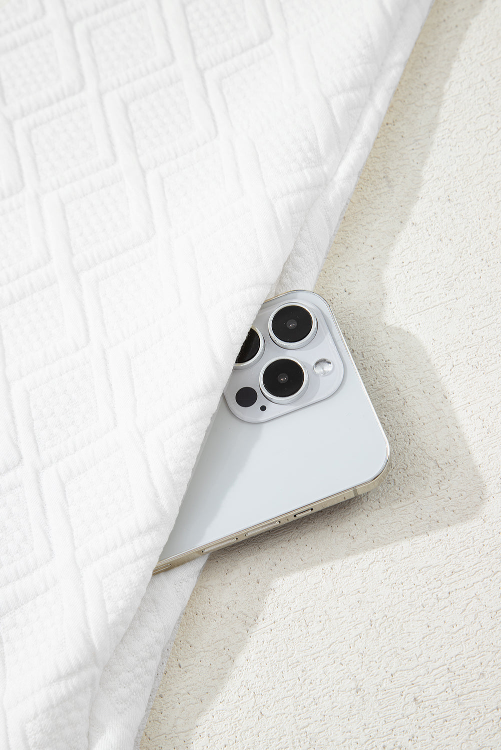 White smartphone partially covered by textured white quilted fabric on light surface