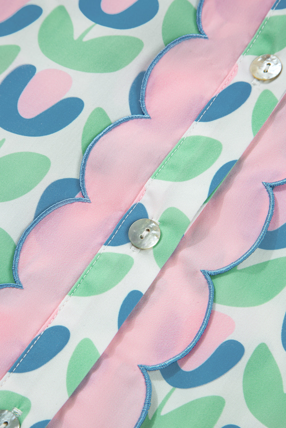 Close-up of a blouse with pastel scalloped trim, floral print, and white buttons