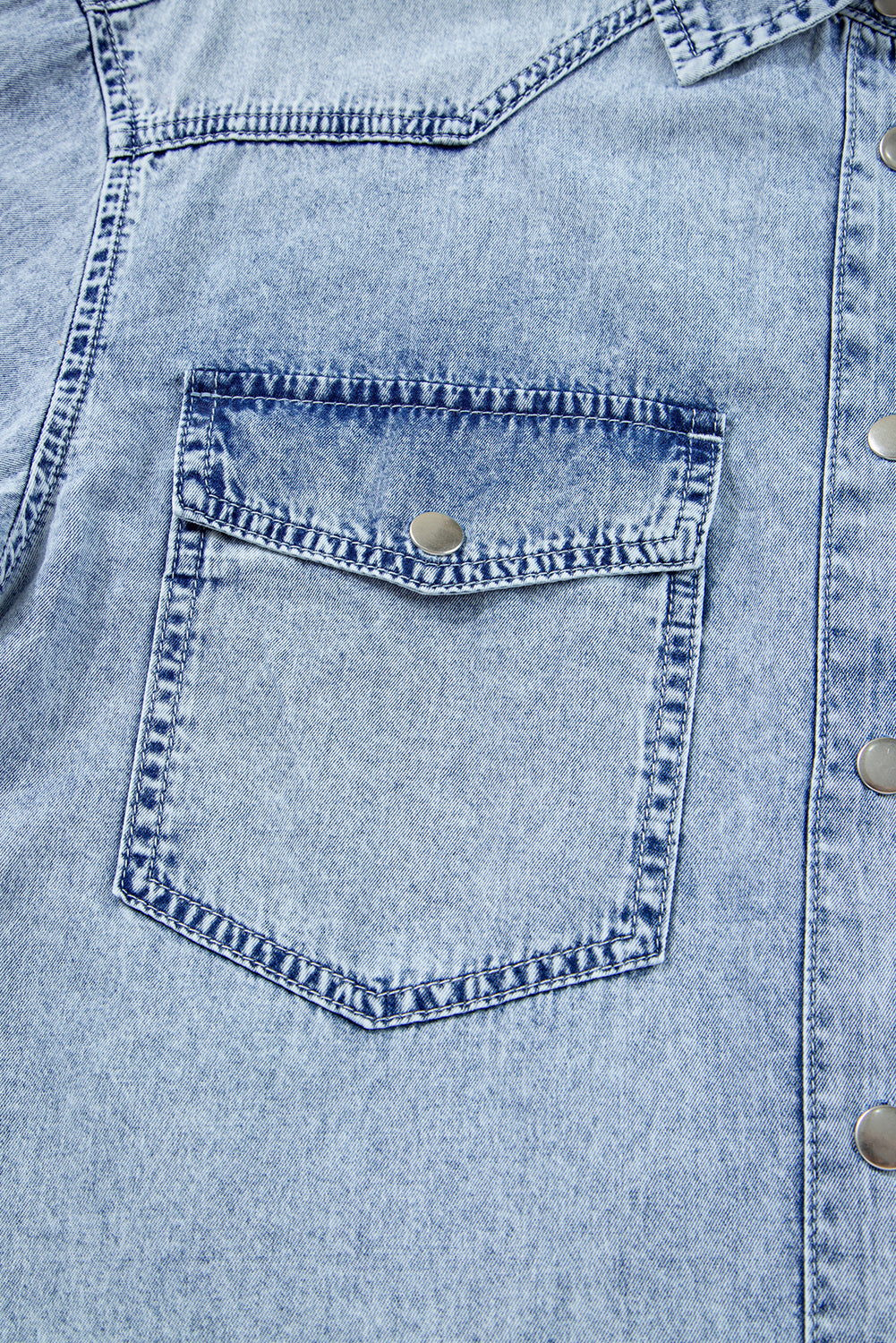 Close-up of light blue denim shirt pocket with metal snap buttons and visible stitching
