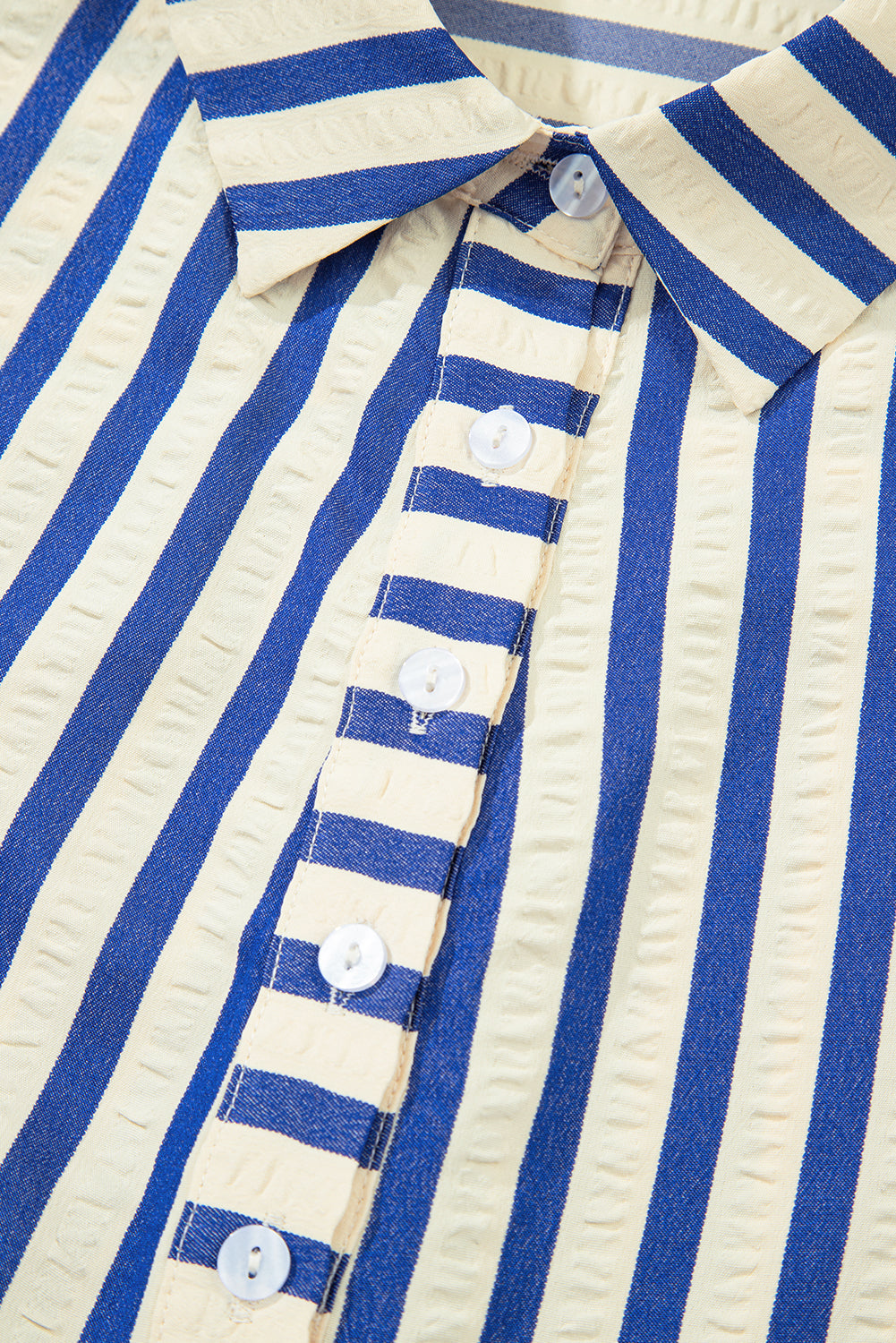Close-up of a blue and cream striped shirt with textured fabric and white buttons