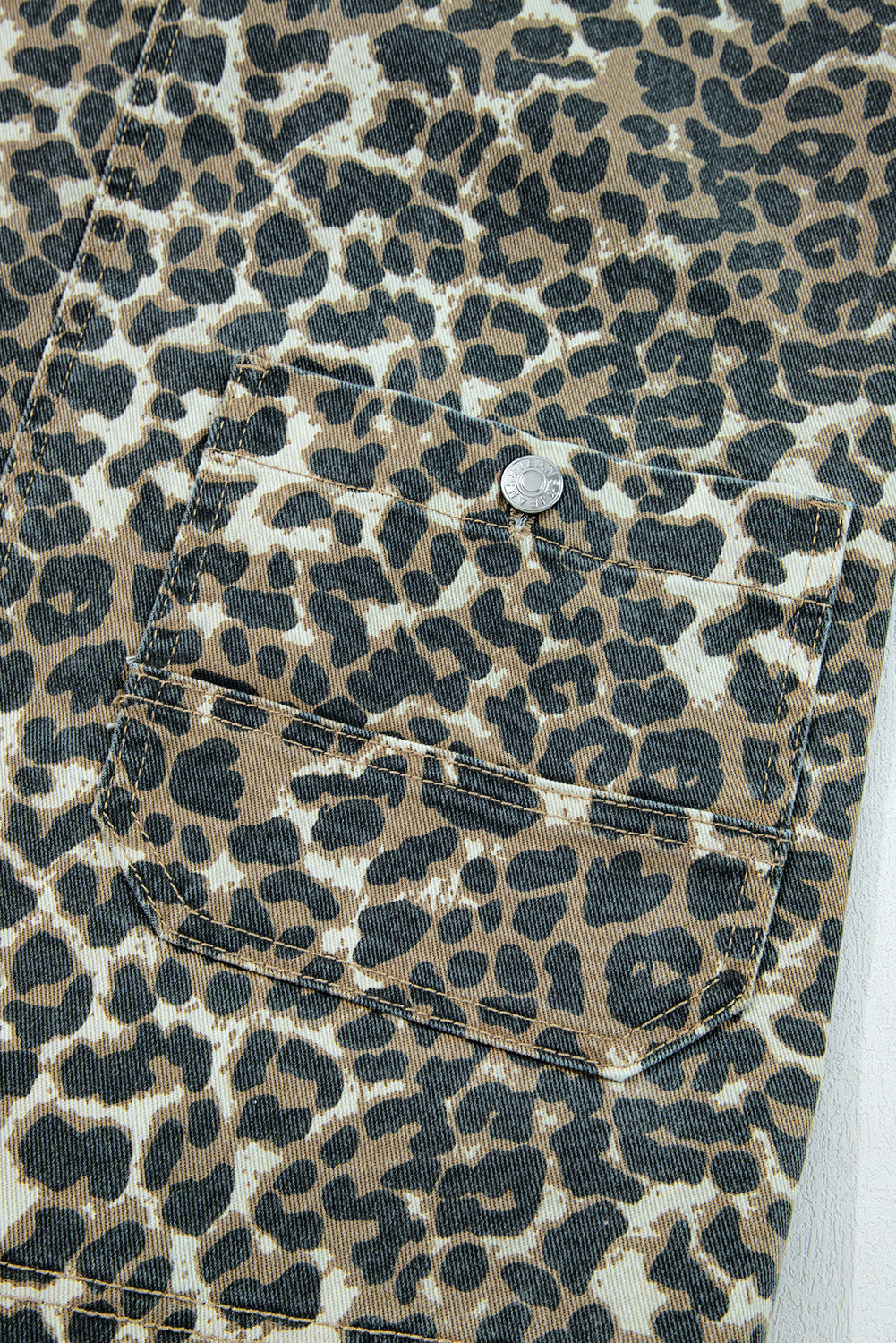 Close-up of leopard print denim fabric with front pocket and metallic button