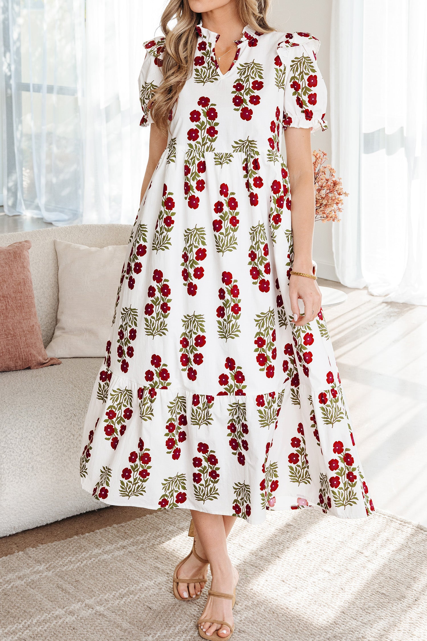 Woman wearing a white floral midi dress with red and green flower print, puff sleeves, and ruffle details
