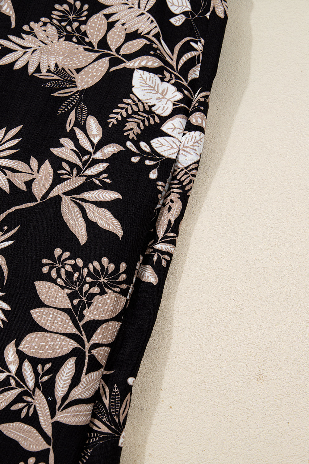Black fabric with beige and white floral botanical print pattern, close-up view