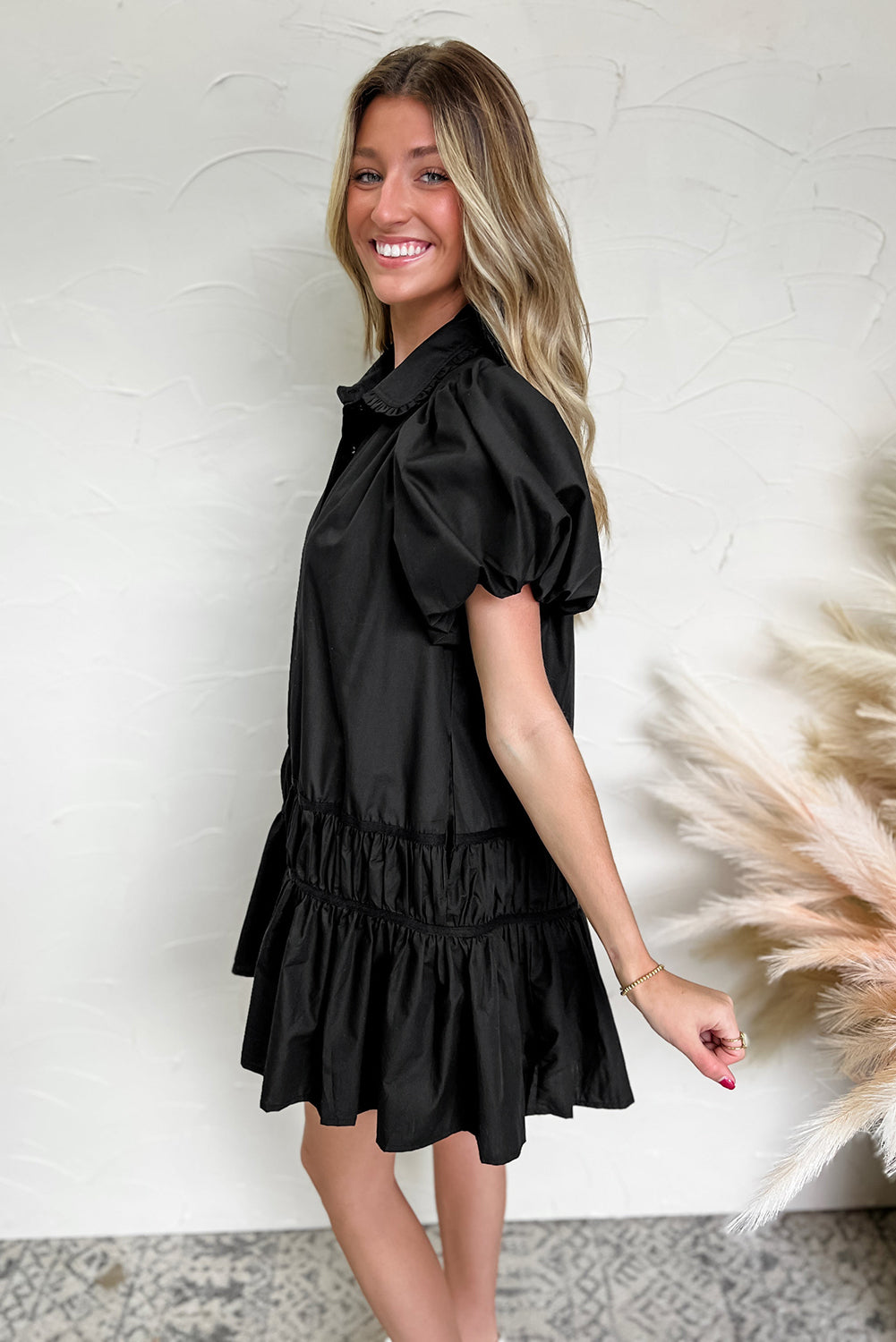 Woman wearing a black puff sleeve mini dress with ruffle details, smiling indoors