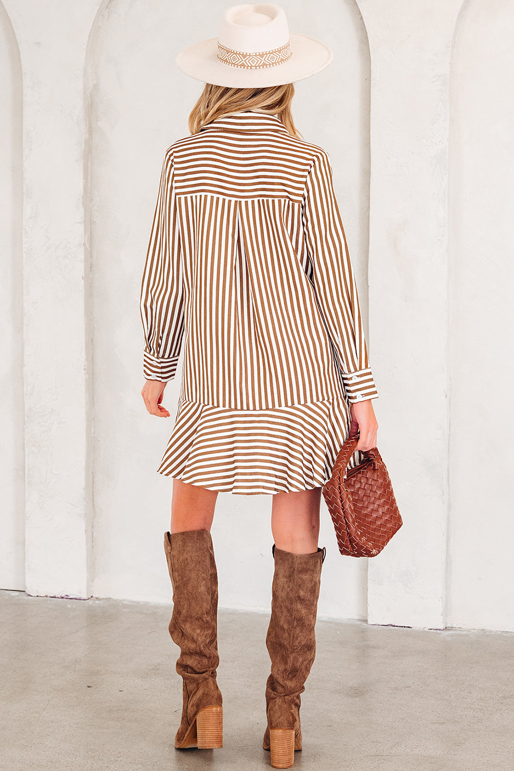 Woman in brown striped shirt dress, suede knee boots, and white hat holding woven bag