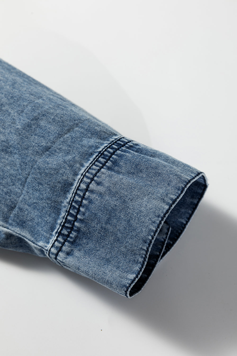 Close-up of a blue denim shirt sleeve with visible stitching on a white background
