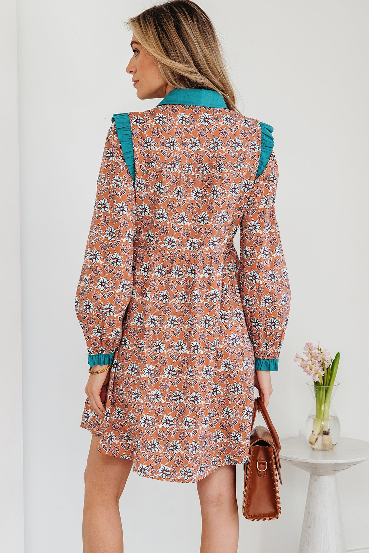 Woman wearing a floral print long sleeve dress with teal accents, holding a brown handbag