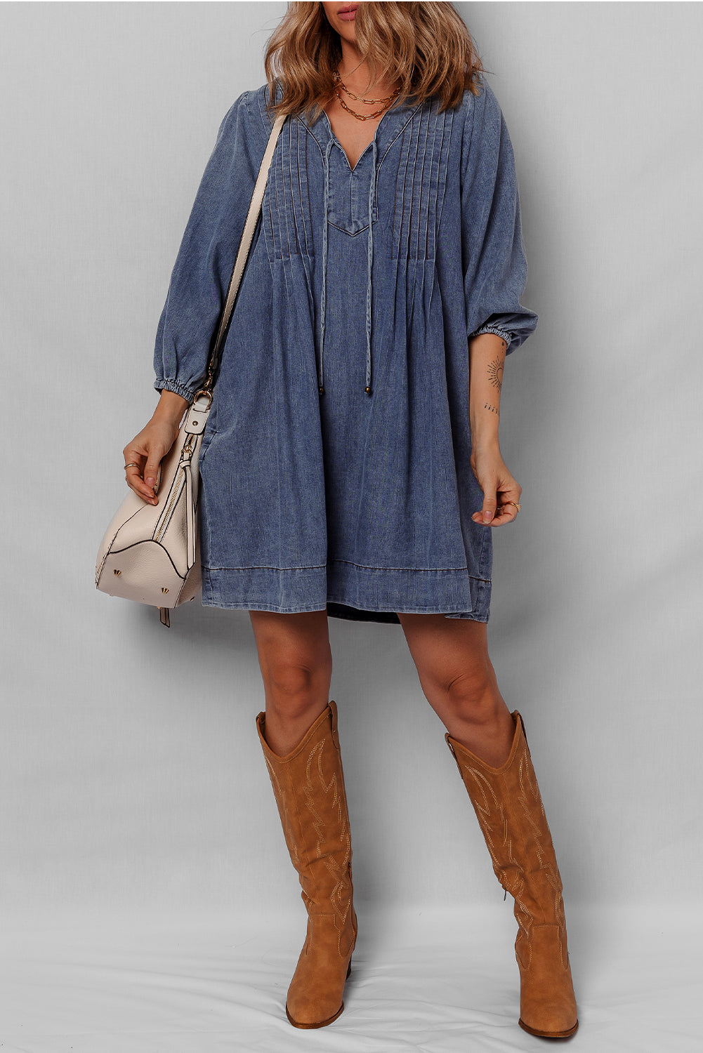 Woman wearing a loose denim dress, tan cowboy boots, and a light beige handbag