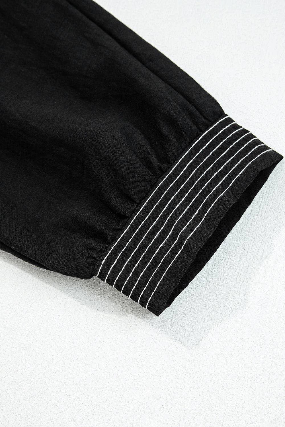 Black long sleeve with white stitched cuff detail on textured surface