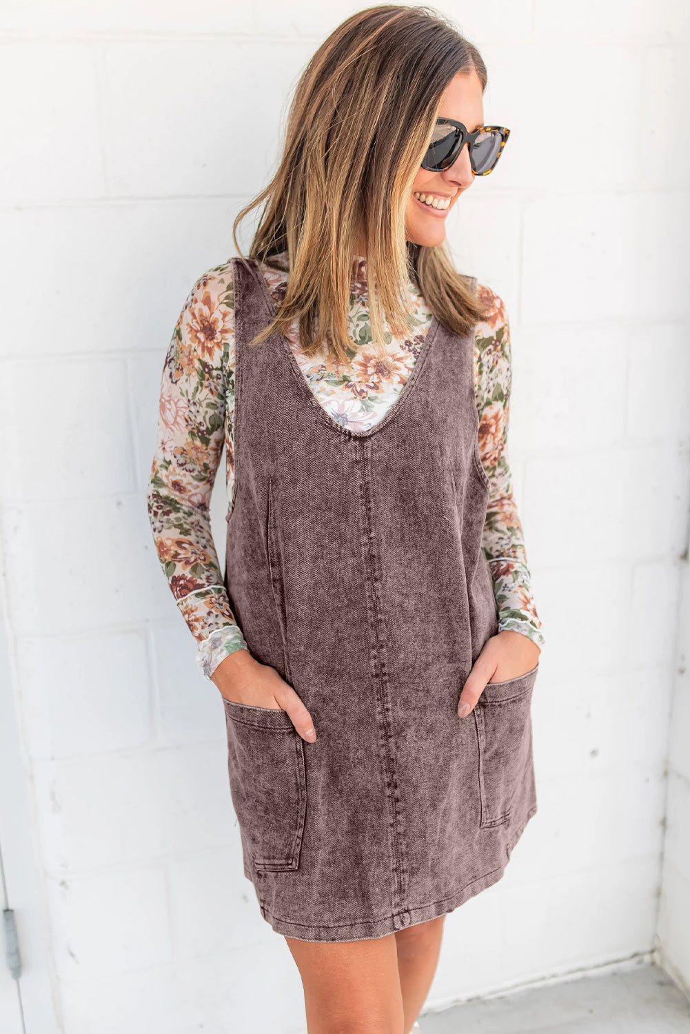 Woman wearing a floral long sleeve top under a sleeveless brown corduroy dress with pockets