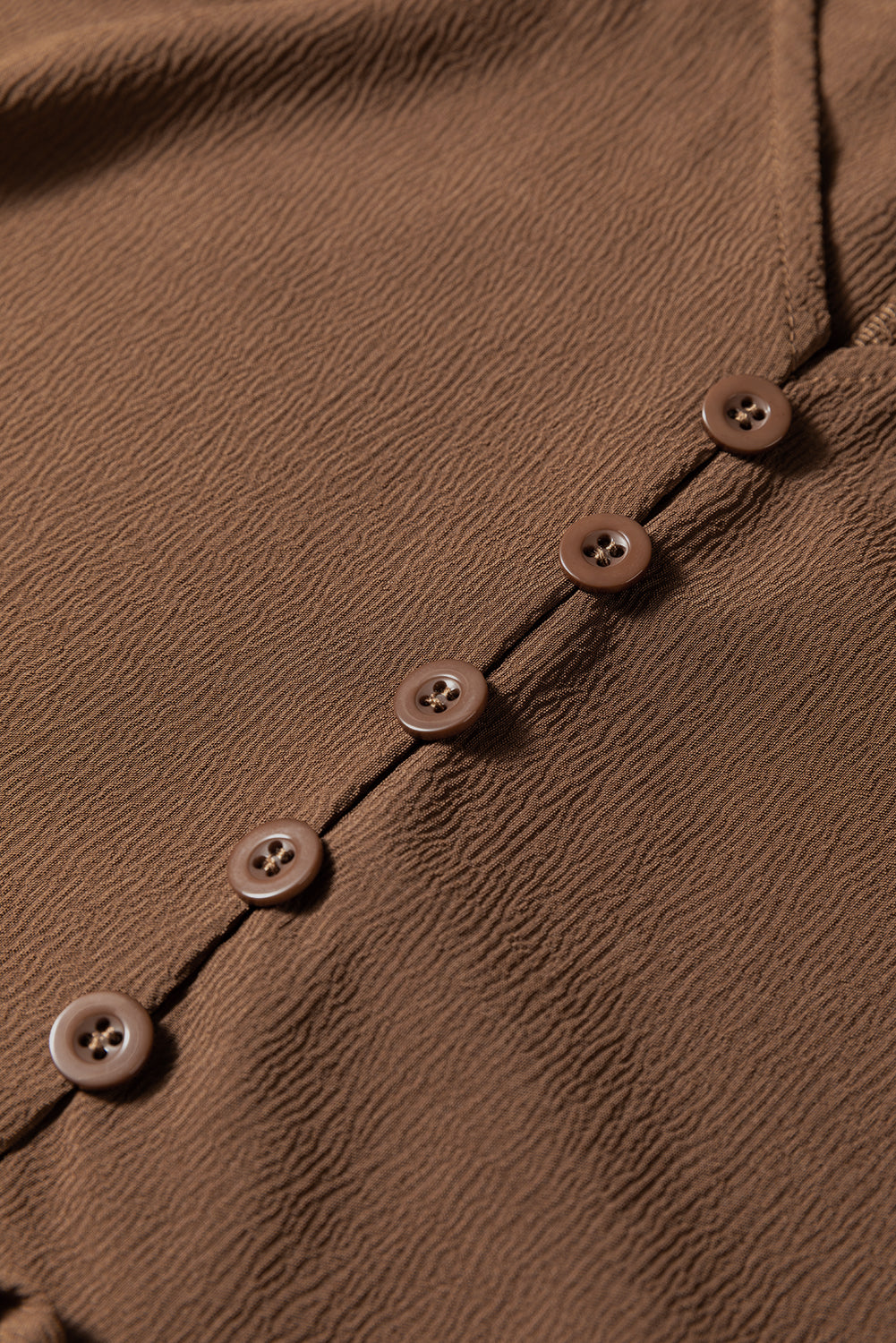 Close-up of a brown textured fabric garment with brown buttons in a row
