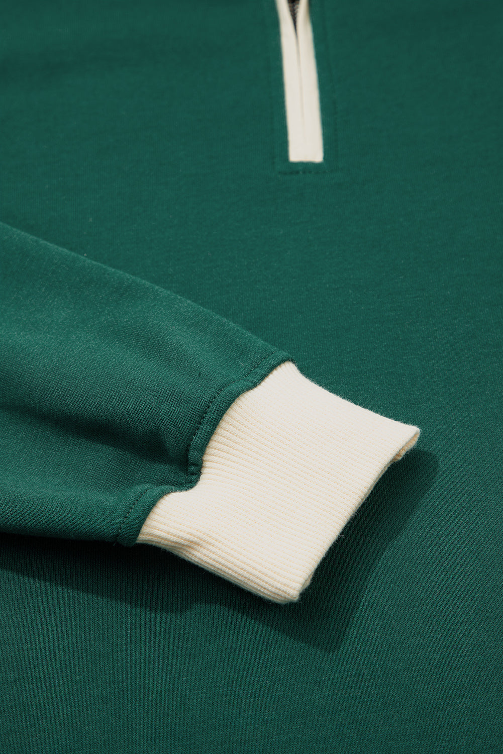 Green quarter-zip sweatshirt with white ribbed cuff and zipper detail, close-up view