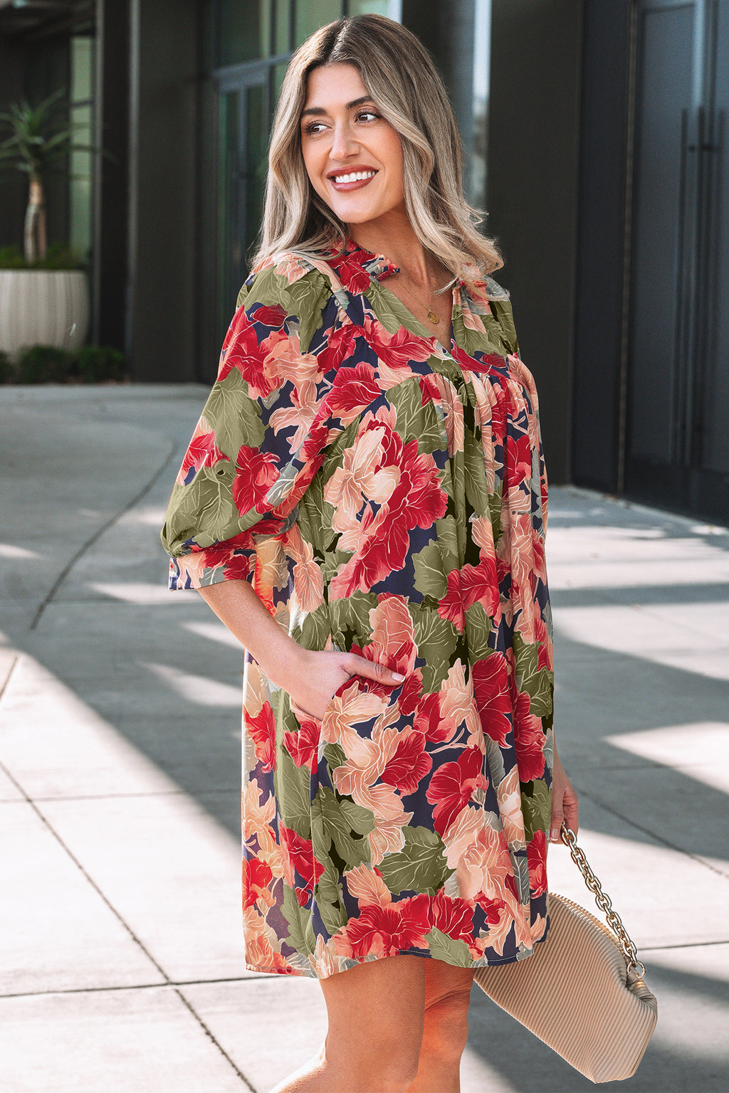 Woman in colorful floral print dress with puff sleeves holding a beige handbag outdoors