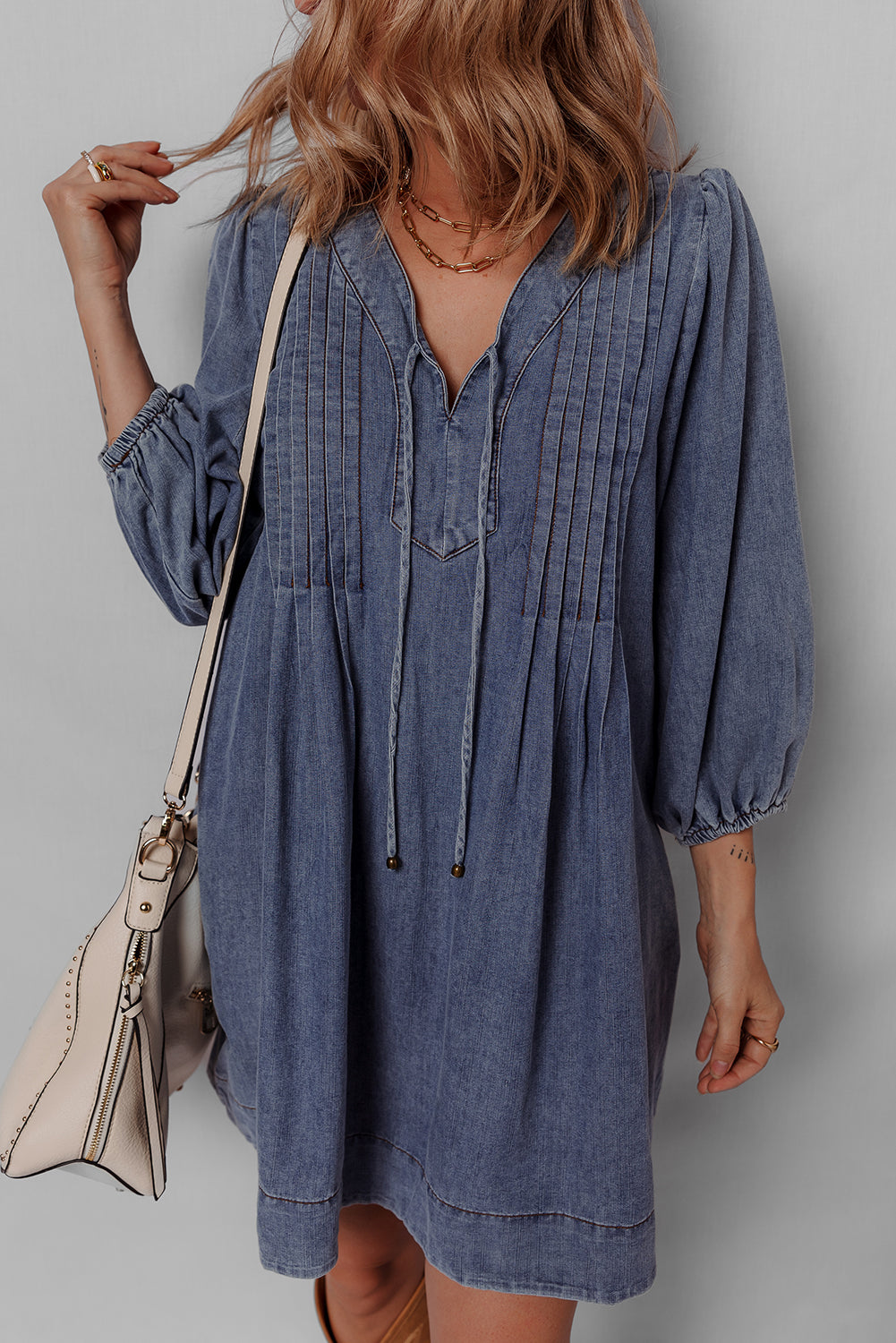 Woman wearing a casual denim dress with puff sleeves and a beige shoulder bag
